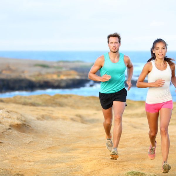 Sports couple jogging for fitness running in beautiful landscape nature outdoors. Young female and male sports athletes training cross-country trail running. Asian woman, Caucasian man,